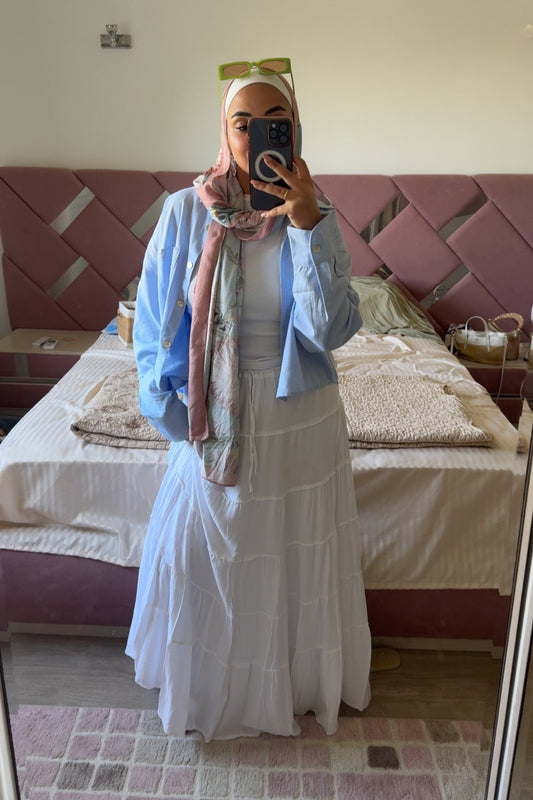 Person wearing a light blue cardigan over a white dress in a bedroom.