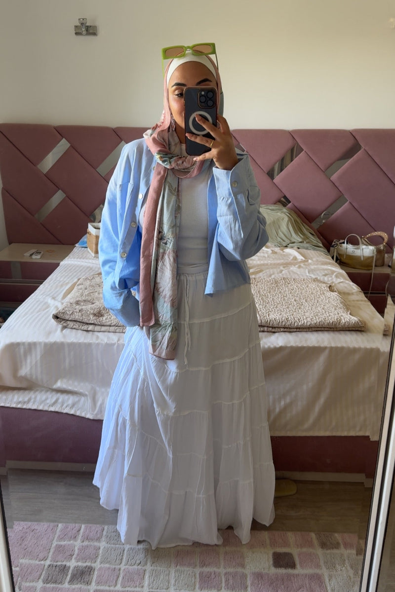 Person wearing a light blue cardigan over a white dress in a bedroom.